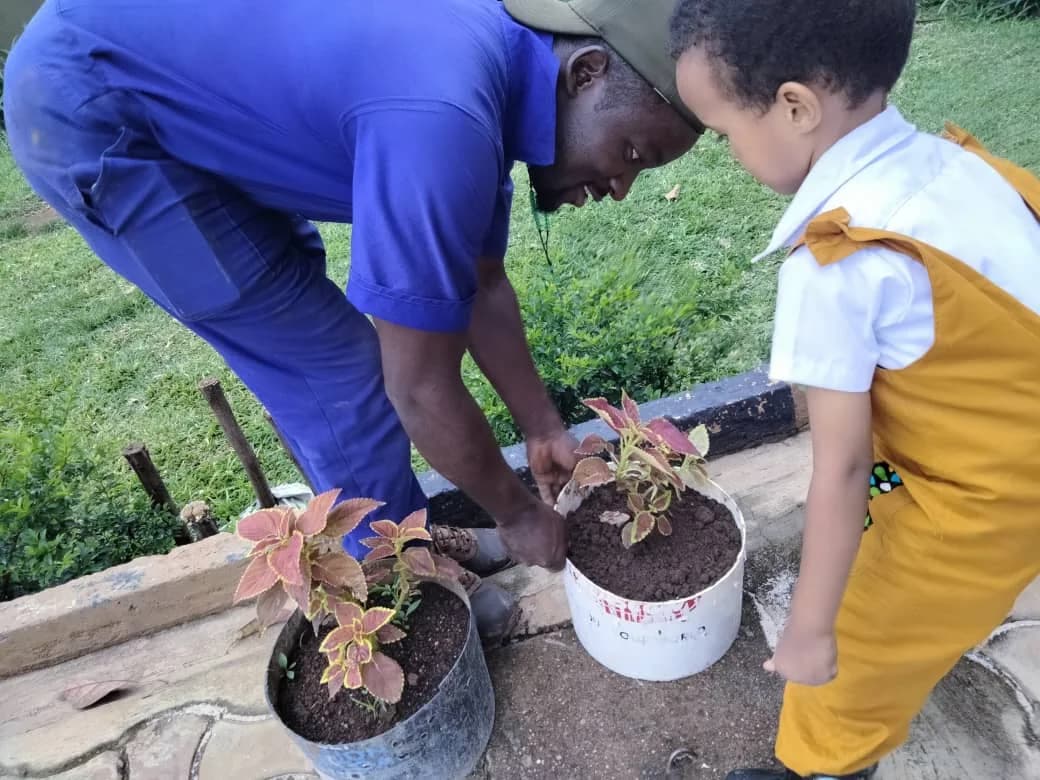 An adult helping an Eco-Bloom child plant a seedling in a pot